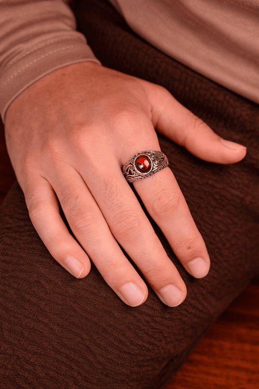 A man wearing a premium red Garnet stone ring with a silver-finish stainless steel band featuring intricate filigree patterns.