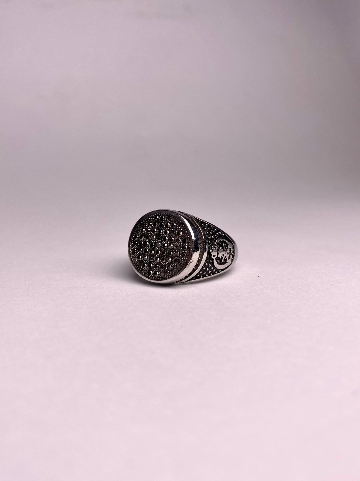 Close-up angled view of a men's oval statement ring with black cubical zircon stones and a textured antique silver-tone finish.