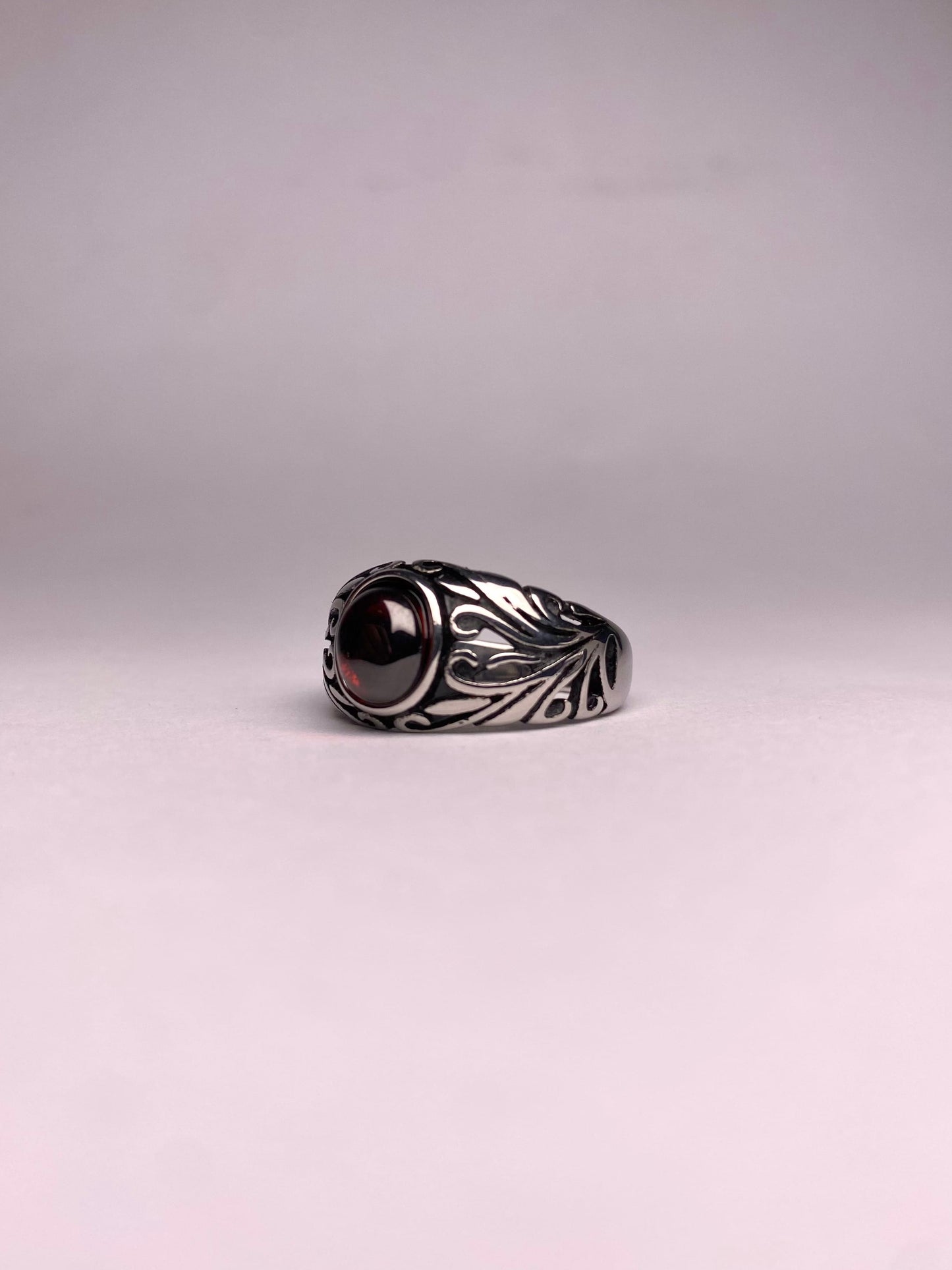 Angle view of a polished dark red Garnet gemstone set in a vintage-style stainless steel ring for a bold masculine look.