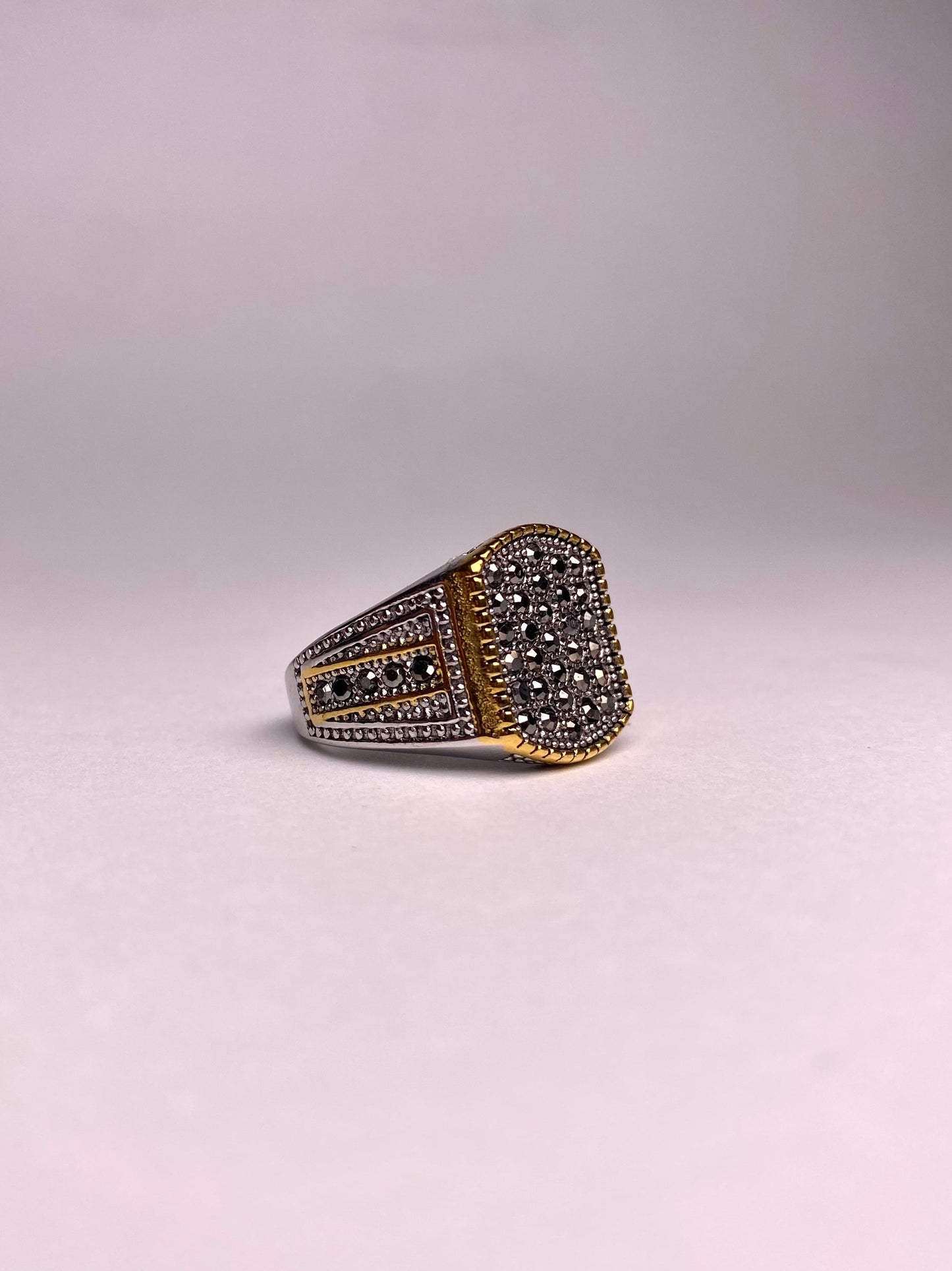 Side view showing the detailed artisan engravings on a gold-finish stainless steel ring with a shimmering black cubical zircon stone.